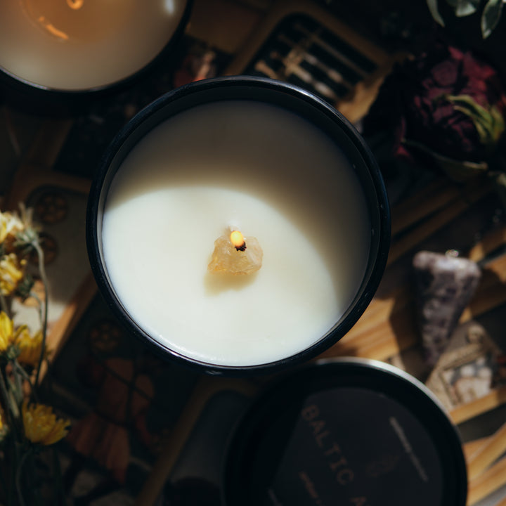 View from the top of the black jar with the wick lit, next to flowers and a black tin lid.