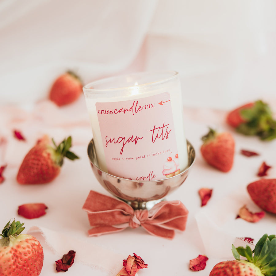 Candle with strawberries and a bow on a white surface next to scattered rose petals