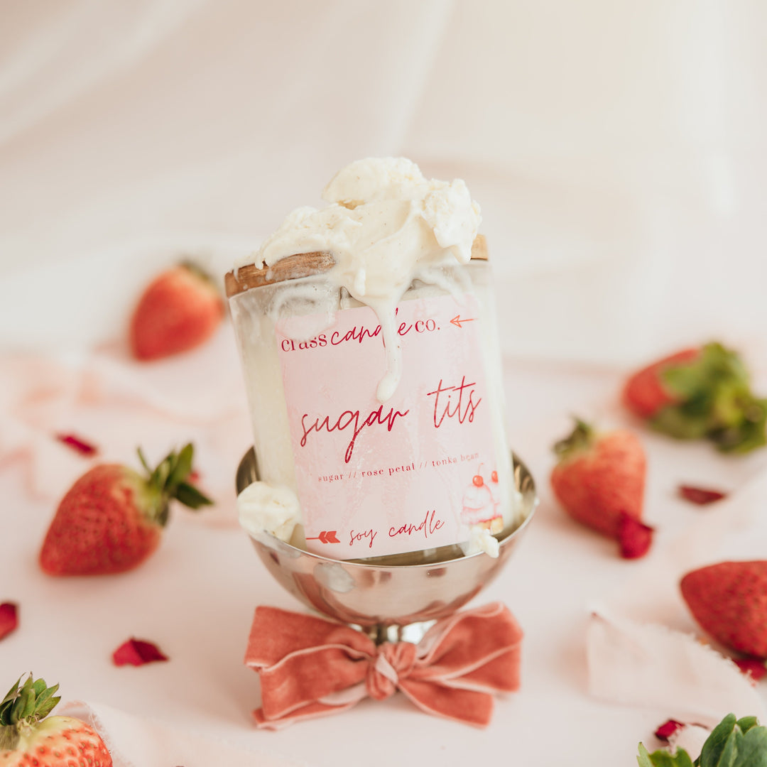 Candle labeled 'sugar tits' being lit with strawberries around on a white surface
