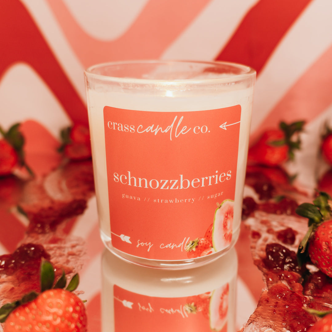 Candle with 'schnozzberries' label surrounded by strawberries on a decorative background