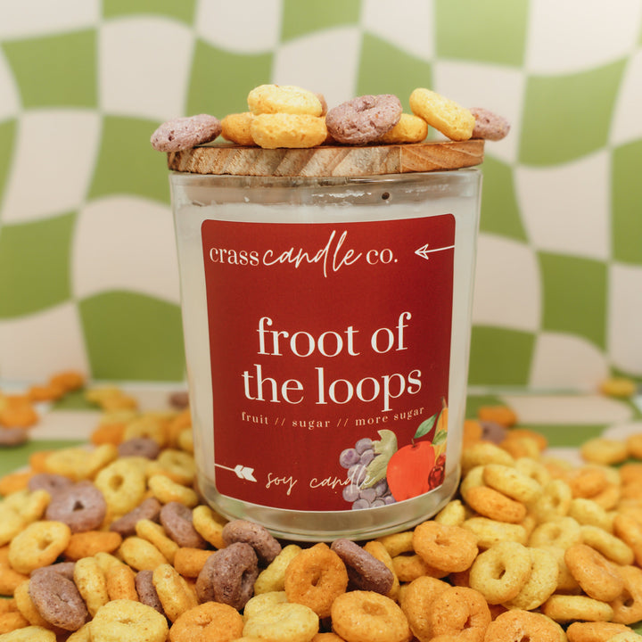Candle labeled 'froot of the loops' surrounded by Froot Loops cereal on a green checkered background