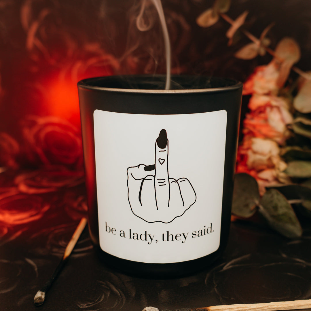Candle with a label featuring a hand gesture and text, surrounded by smoke and leaves.